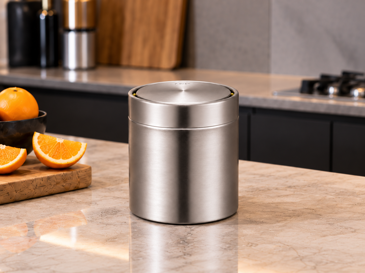 EKO Fandy 1.5L Stainless Steel Kitchen Countertop Bin Compact EKO Fandy stainless steel swing-top mini bin on a modern kitchen island beside a wooden cutting board and oranges.