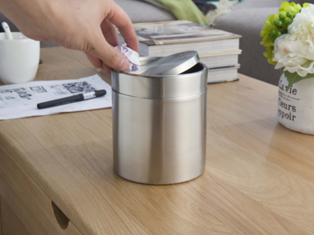 Hand disposing of a crumpled paper into the EKO Fandy stainless steel table bin, demonstrating its swing-top lid.